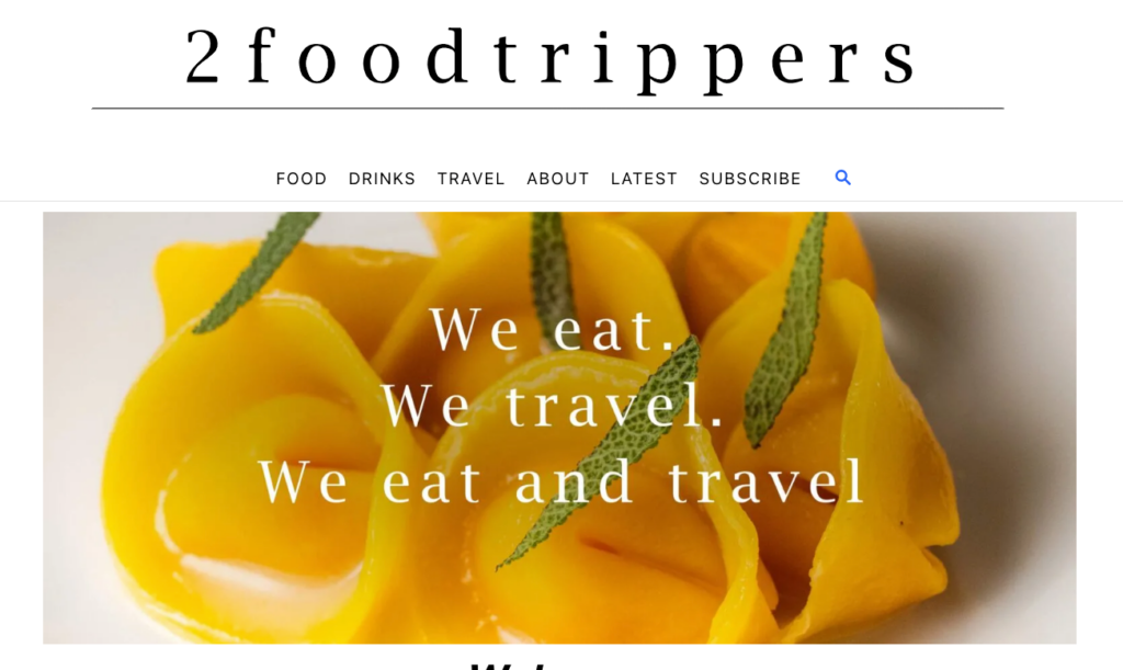 The image displays the homepage of travel food bloggers, 2foodtrippers. The picture shows bright, yellow food with text saying, “We eat, We travel, We eat and travel.”