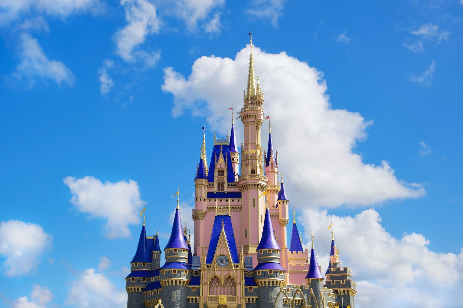 A snapshot of the pink, blue, and gold castle in Walt Disney World against a blue sky and white clouds.