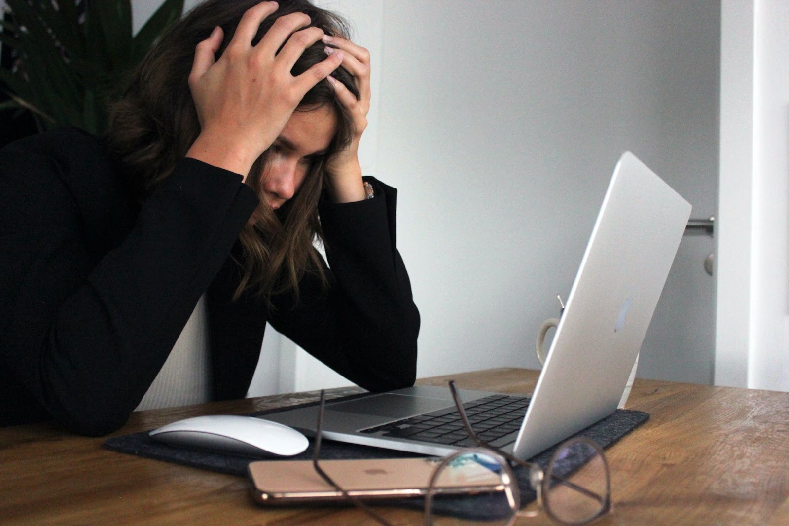 A woman in a black sweater sitting with her head in her hands, looking at her computer screen with a frustrated facial expression.